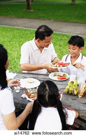 Family sitting at picnic table, father passing son food View Large Photo Image Stock Image - Family sitting at picnic table, father passing son food. Fotosearch