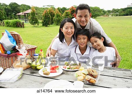 Picture - Family sitting at picnic table, looking at camera, portrait. Fotosearch