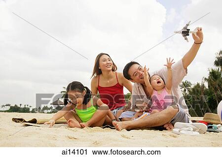 Stock Image - Family two children, playing on beach with toy boat and toy plane. Fotosearch