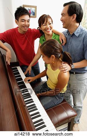 Stock Photo - Family with two children, standing around piano, daughter playing piano. Fotosearch