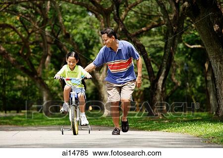 Father and daughter in park, daughter cycling, father running alongside her View Large Photo Image Stock Photography - Father and daughter in park, daughter cycling, father running alongside her. Fotosearch