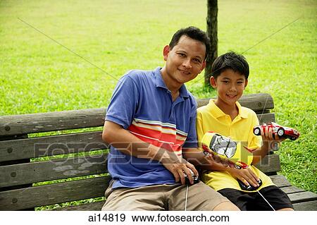 Stock Photo - Father and son holding remote control cars, smiling. Fotosearch
