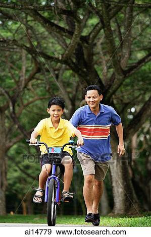 Father and son in park, son cycling, father running behind him View Large Photo Image Stock Photo - Father and son in park, son cycling, father running behind him. Fotosearch