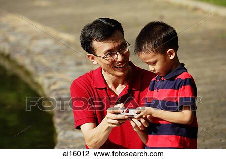 Stock Image - Father and son looking at remote control. Fotosearch
