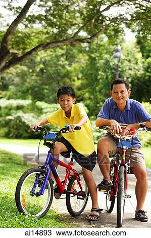 Stock Image - Father and son on bicycle, looking at camera. Fotosearch