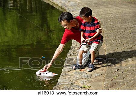 Stock Image - Father and son playing with remote control boat, father reaching for boat. Fotosearch