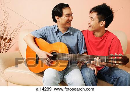Stock Photo - Father and son side by side, holding guitar, looking at each other. Fotosearch