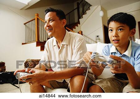 Father and son, side by side, playing video games View Large Photo Image Picture - Father and son, side by side, playing video games. Fotosearch