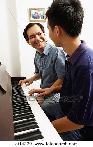 Stock Image - Father and son sitting at piano, looking at each other. Fotosearch