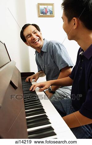 Stock Photo - Father and son sitting at piano, looking at each other. Fotosearch