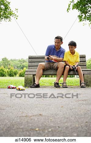 Father and son, sitting on bench, playing with remote control cars View Large Photo Image Stock Photograph - Father and son, sitting on bench, playing with remote control cars. Fotosearch