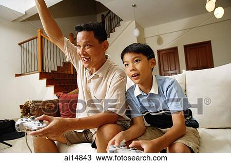 Father and son, sitting on sofa, holding video game controllers, father with arm raised View Large Photo Image Stock Image - Father and son, sitting on sofa, holding video game controllers, father with arm raised. Fotosearch