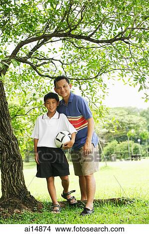 Father and son standing under tree, looking at camera View Large Photo Image Picture - Father and son standing under tree, looking at camera. Fotosearch