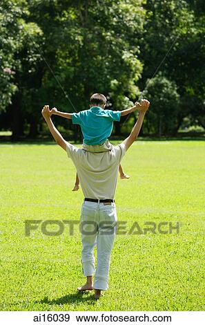 Stock Photo - Father carrying son on shoulders, walking in field. Fotosearch