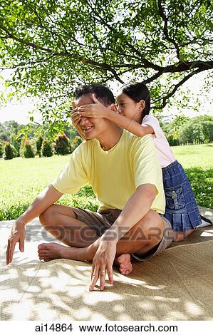 Father sitting on mat, daughter behind him, covering his eyes with her hands View Large Photo Image Picture - Father sitting on mat, daughter behind him, covering his eyes with her hands. Fotosearch