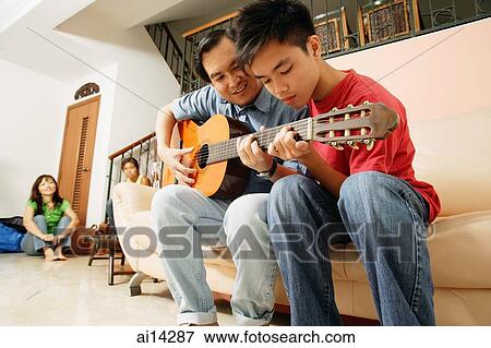 Father teaching son to play guitar, mother and daughter in the background View Large Photo Image Stock Photo - Father teaching son to play guitar, mother and daughter in the background. Fotosearch