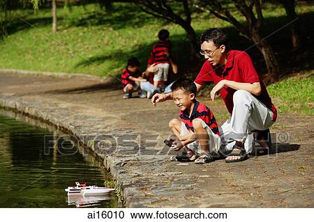 Stock Image - Father with son, playing with remote control boat. Fotosearch