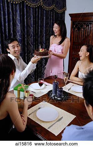 Friends around dining table, woman passing cake to man at head of table View Large Photo Image Stock Photograph - Friends around dining table, woman passing cake to man at head of table. Fotosearch
