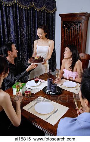 Friends around dining table, woman serving cake to man at head of table View Large Photo Image Stock Photography - Friends around dining table, woman serving cake to man at head of table. Fotosearch