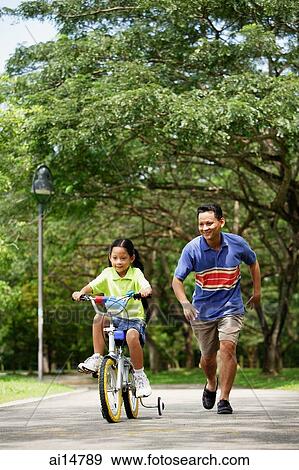 Girl cycling away, father running behind her View Large Photo Image Stock Photo - Girl cycling away, father running behind her. Fotosearch