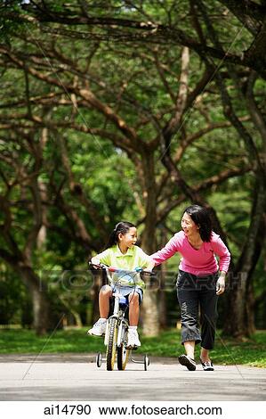 Girl cycling, mother walking next to her View Large Photo Image Stock Image - Girl cycling, mother walking next to her. Fotosearch