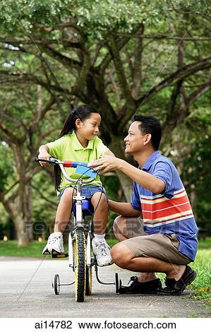 Girl on bicycle, father crouching down next to her View Large Photo Image Stock Image - Girl on bicycle, father crouching down next to her. Fotosearch
