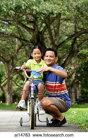 Girl on bicycle, father crouching down next to her, both looking at camera View Large Photo Image Stock Image - Girl on bicycle, father crouching down next to her, both looking at camera. Fotosearch