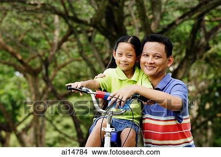 Picture - Girl on bicycle, father next to her, both looking at camera. Fotosearch