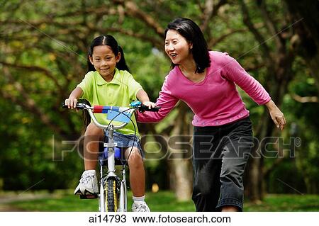 Girl on cycling, mother next to her, holding her View Large Photo Image Stock Image - Girl on cycling, mother next to her, holding her. Fotosearch