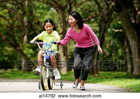 Girl on training bicycle, mother guiding her View Large Photo Image Stock Image - Girl on training bicycle, mother guiding her. Fotosearch