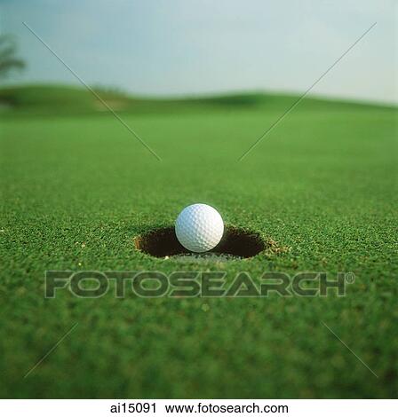 Stock Image - Golf ball dropping in to hole. Fotosearch