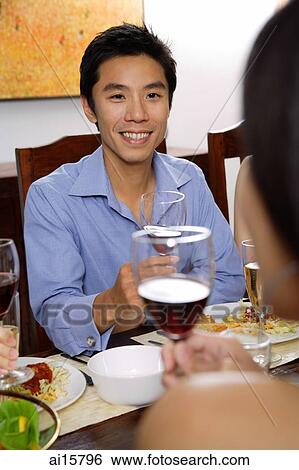 Stock Photograph - Man at dinner table, holding wine glasses, facing another person. Fotosearch