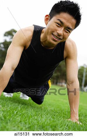 Stock Image - Man doing push-ups on grass, looking at camera. Fotosearch