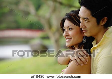 Man embracing woman from behind, arm around her shoulder, both looking away View Large Photo Image Stock Image - Man embracing woman from behind, arm around her shoulder, both looking away. Fotosearch