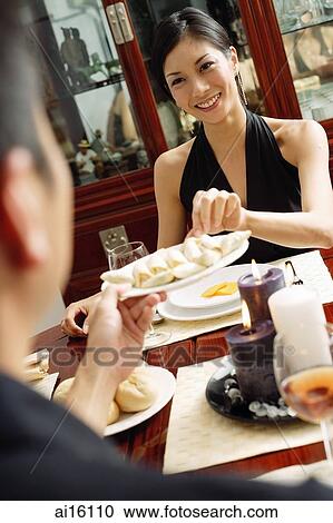 Stock Image - Man holding plate of food, woman taking from it. Fotosearch