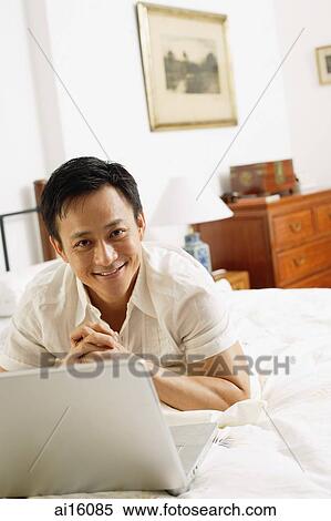 Man in bedroom, using laptop, hands clasped, looking at camera View Large Photo Image Stock Photography - Man in bedroom, using laptop, hands clasped, looking at camera. Fotosearch