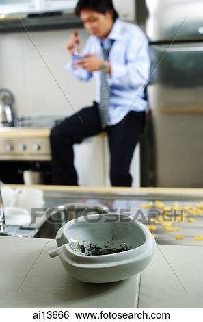 Man in kitchen, ashtray and cigarette in foreground ( selective focus) View Large Photo Image Stock Photograph - Man in kitchen, ashtray and cigarette in foreground ( selective focus). Fotosearch