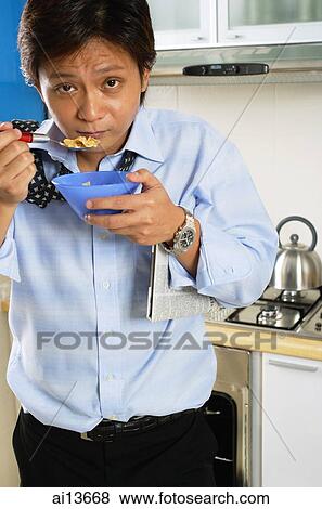 Man in kitchen, eating bowl of cereal, looking at camera View Large Photo Image Stock Photo - Man in kitchen, eating bowl of cereal, looking at camera. Fotosearch