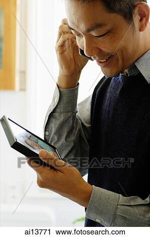 Stock Image - Man looking at picture frame and using mobile phone. Fotosearch