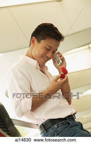 Man looking at ring box, using mobile phone, smiling View Large Photo Image Stock Image - Man looking at ring box, using mobile phone, smiling. Fotosearch