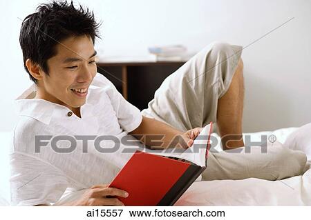 Man lying on bed, reading book, smiling View Large Photo Image Stock Photo - Man lying on bed, reading book, smiling. Fotosearch