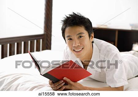 Man lying on bed, reading book, smiling at camera View Large Photo Image Stock Photo - Man lying on bed, reading book, smiling at camera. Fotosearch