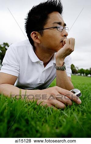 Man lying on grass, holding handphone, hand on chin, looking away View Large Photo Image Stock Photo - Man lying on grass, holding handphone, hand on chin, looking away. Fotosearch