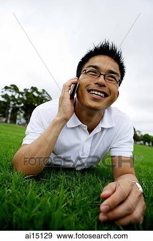 Man lying on grass, using handphone, smiling View Large Photo Image Stock Photo - Man lying on grass, using handphone, smiling. Fotosearch
