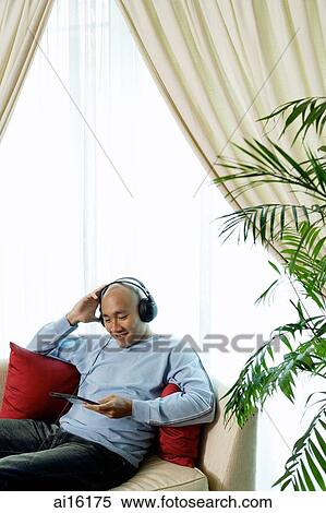 Stock Photography - Man on sofa with headphones, listening to music. Fotosearch