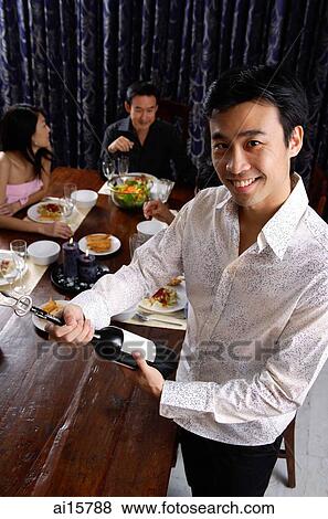 Man opening bottle of wine, smiling at camera, people in the background View Large Photo Image Stock Photo - Man opening bottle of wine, smiling at camera, people in the background. Fotosearch