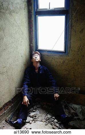 Stock Image - Man sitting in corner of empty room, smoking. Fotosearch