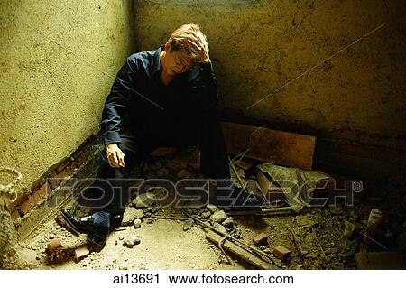 Stock Image - Man sitting in empty room, hand on head. Fotosearch