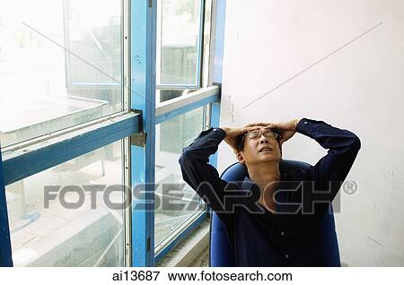Stock Photo - Man sitting on chair, hands on head. Fotosearch