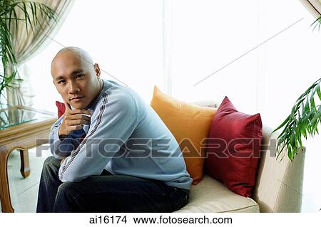Man sitting on sofa in living room, looking at camera View Large Photo Image Picture - Man sitting on sofa in living room, looking at camera. Fotosearch